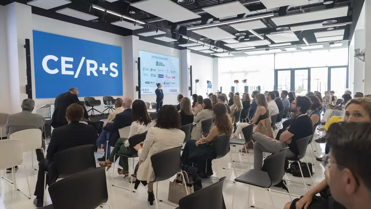 Escenario de una conferencia con ponentes y una gran pantalla de fondo.